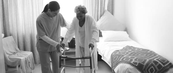 caretaker helps elder woman with walker